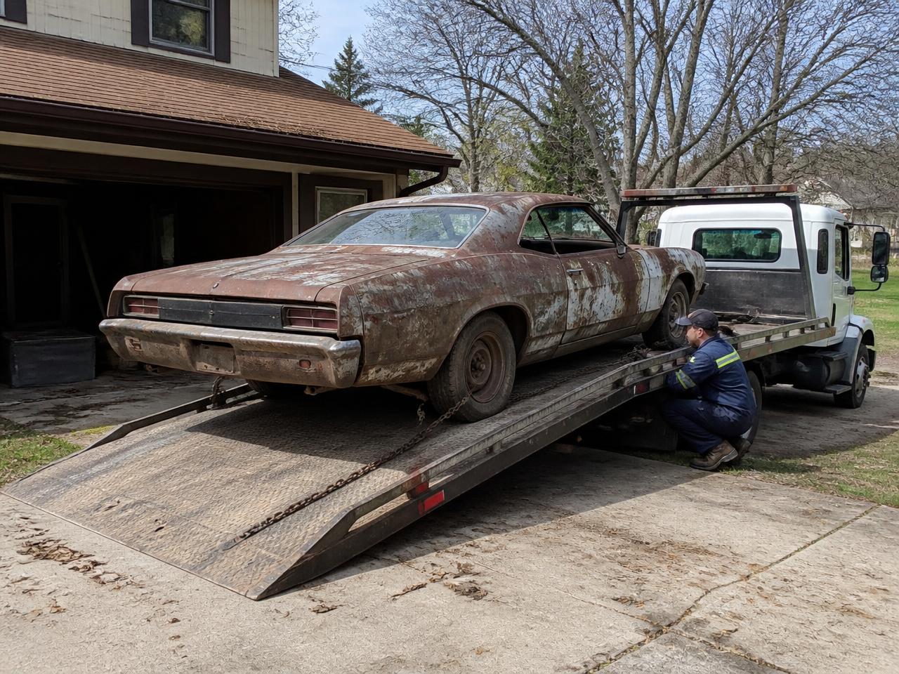 Old rusty junk car being loaded onto a flatbed tow truck in a driveway